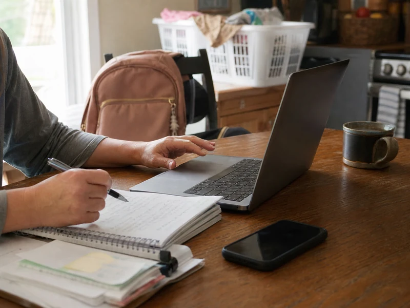A mom reviewing remote job options at a lived-in kitchen table with her phone face down